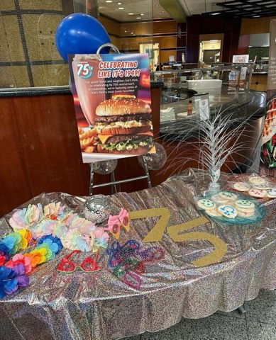 a 75th anniversary standee next to a table with a silver table cloth and the number 75 on it filled with Smiley Cookies