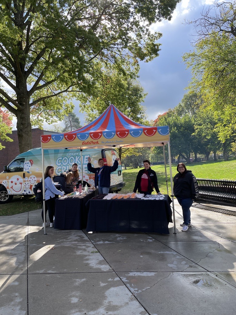 a tent with people and swag like Smiley Cookies, a van decorated with Smiley Cookies in the background