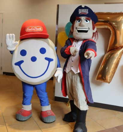 a giant cookie mascot stands next to a colonial man mascot