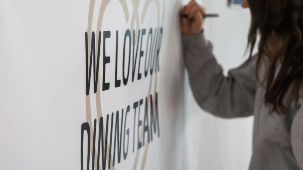 a female college student writes a message on a sign that says We Love Our Dining Team