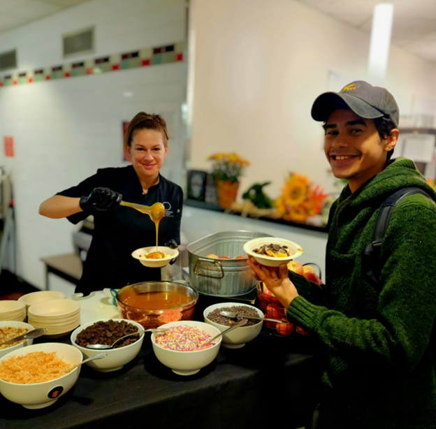 a student and a team member pouring caramel over apples