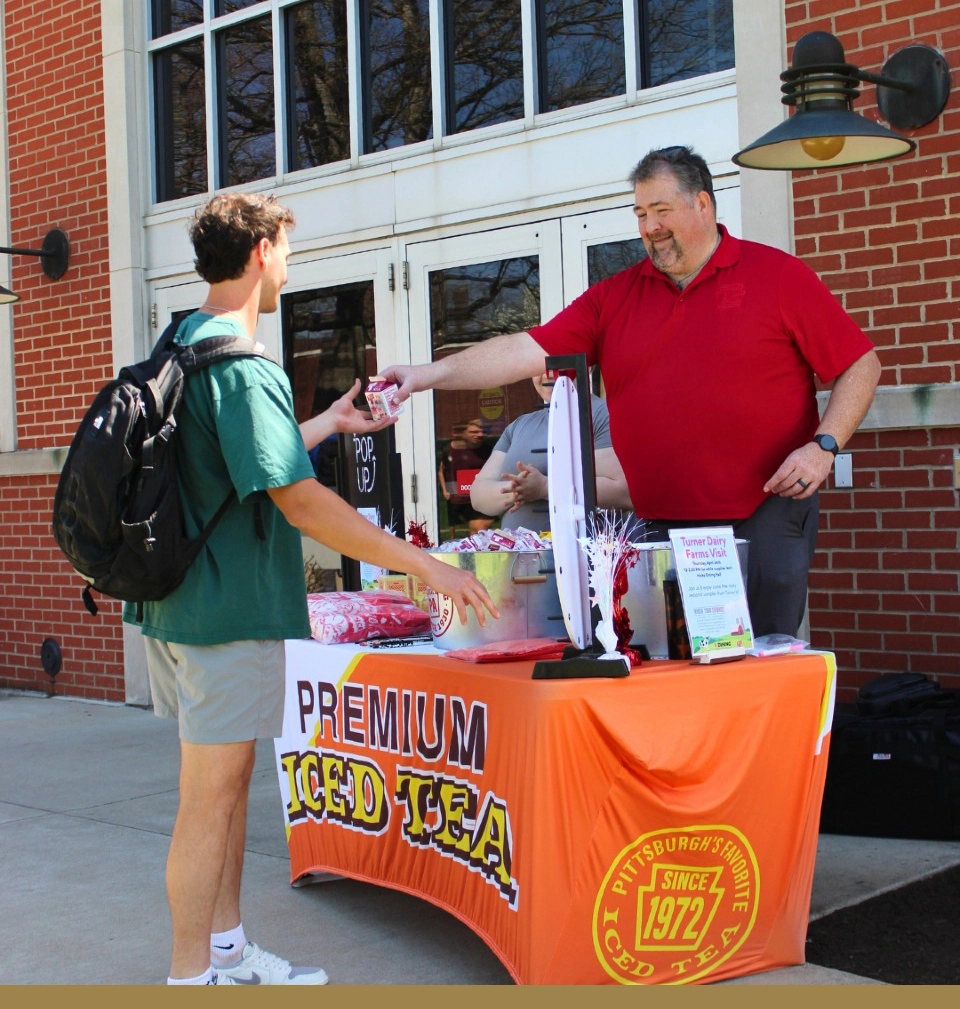 Through the Parkhurst Know Your Source program, a partner has an outdoor stand where he hands his business' iced tea to a student.