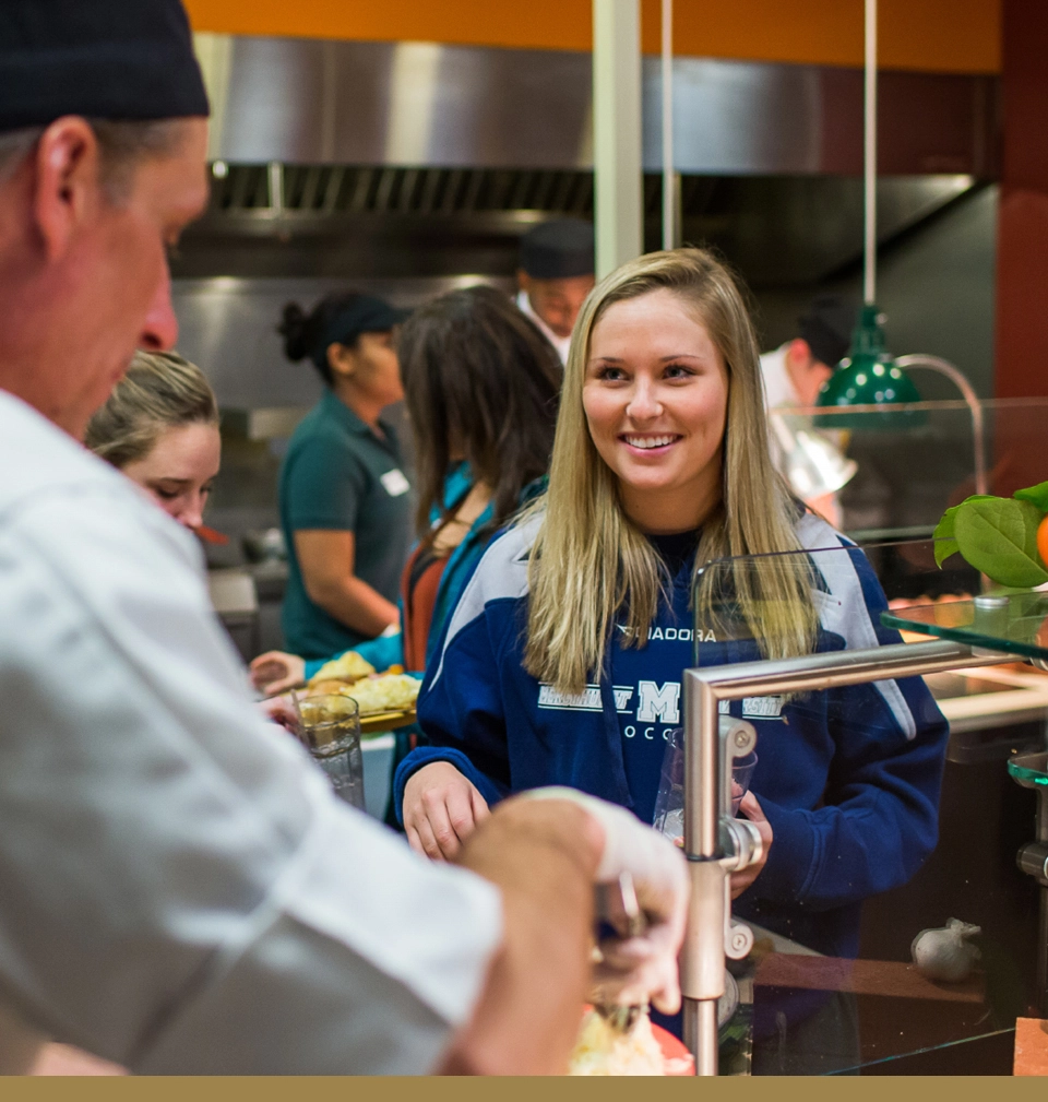 A dining hall guest smiles as she is being served food by a Parkhurst chef.