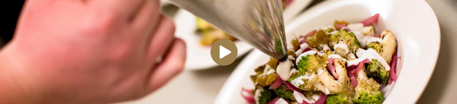 Close up image of Parkhurst chef completing a meal, with play button shown linking to YouTube video.