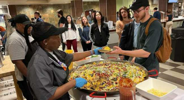 Parkhurst Dining chefs serve higher education students from a large skillet.