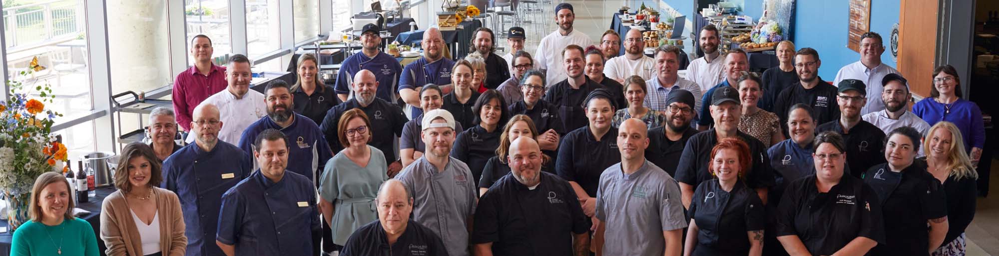 A large group of smiling Parkhurst team members gather in a dining area for a photo highlighting the familial culture between them.