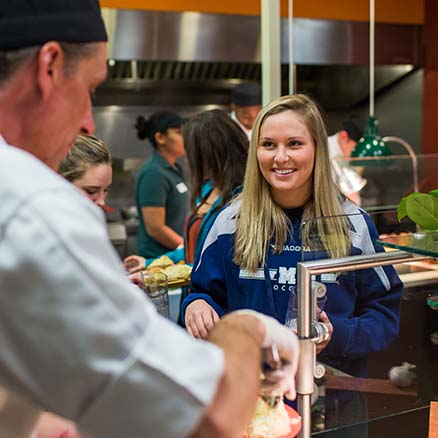 A dining hall guest smiles as she is being served food by a Parkhurst chef.