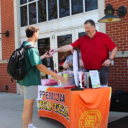 Through the Parkhurst Know Your Source program, a partner has an outdoor stand where he hands his business' iced tea to a student.