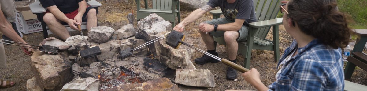chefs sit around a campfire at a camp'n cook event