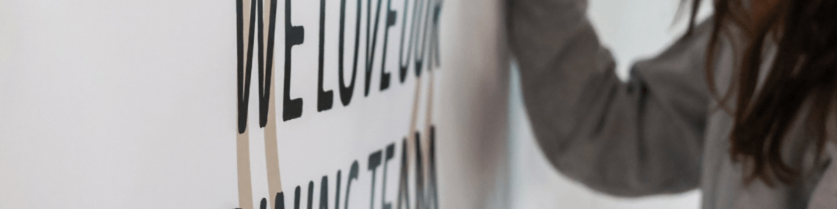 a female college student writes a message on a sign that says We Love Our Dining Team