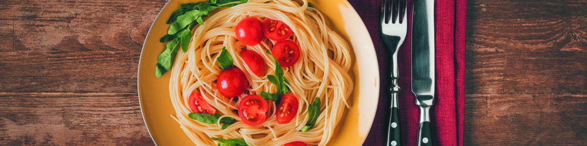 traditional italian pasta with tomatoes and arugula in plate with knife and fork on wooden tabletop
